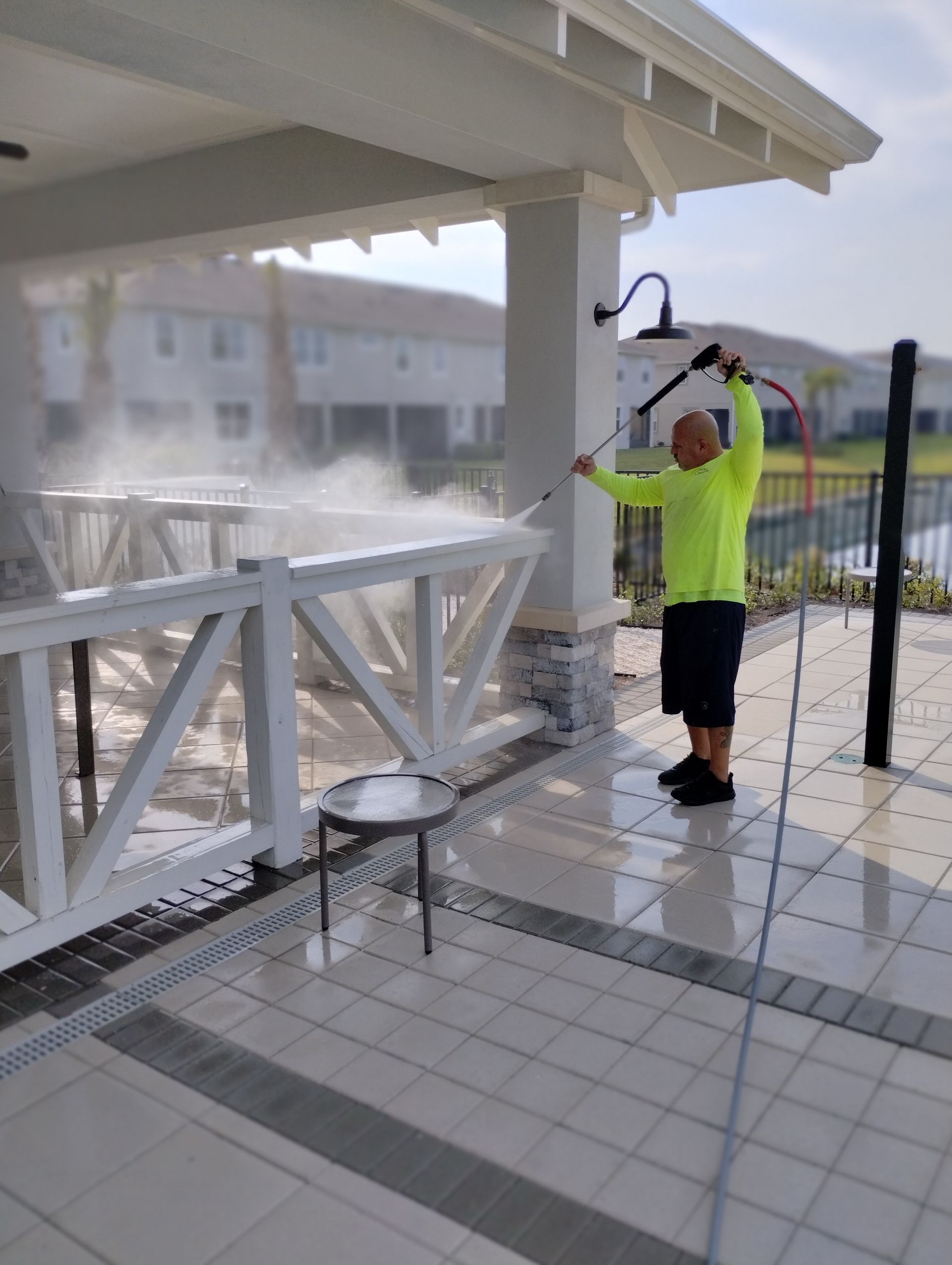Man power washing a white patio under a covered area.