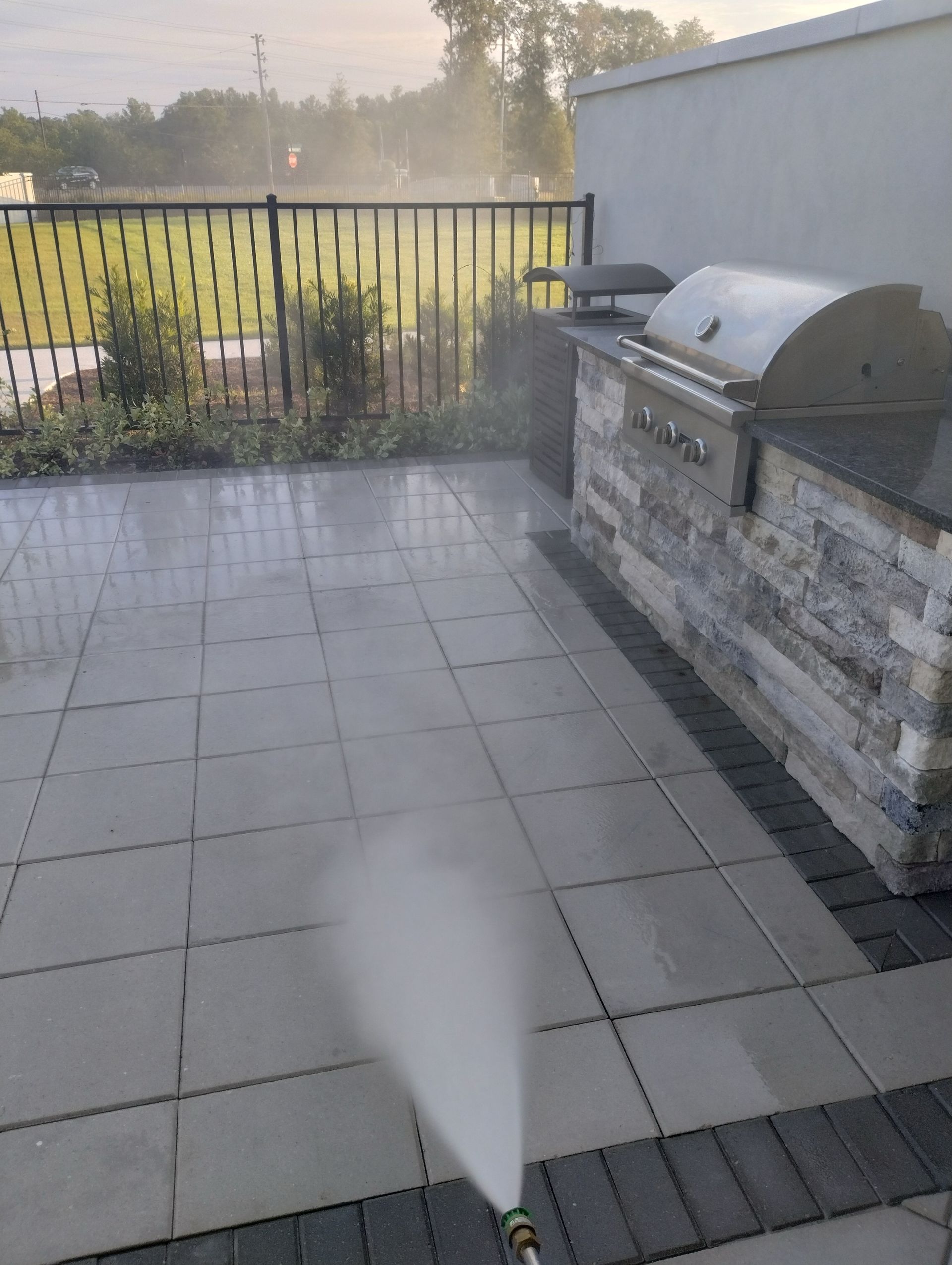 Pressure washing a tiled patio with outdoor kitchen and black fence in the background.