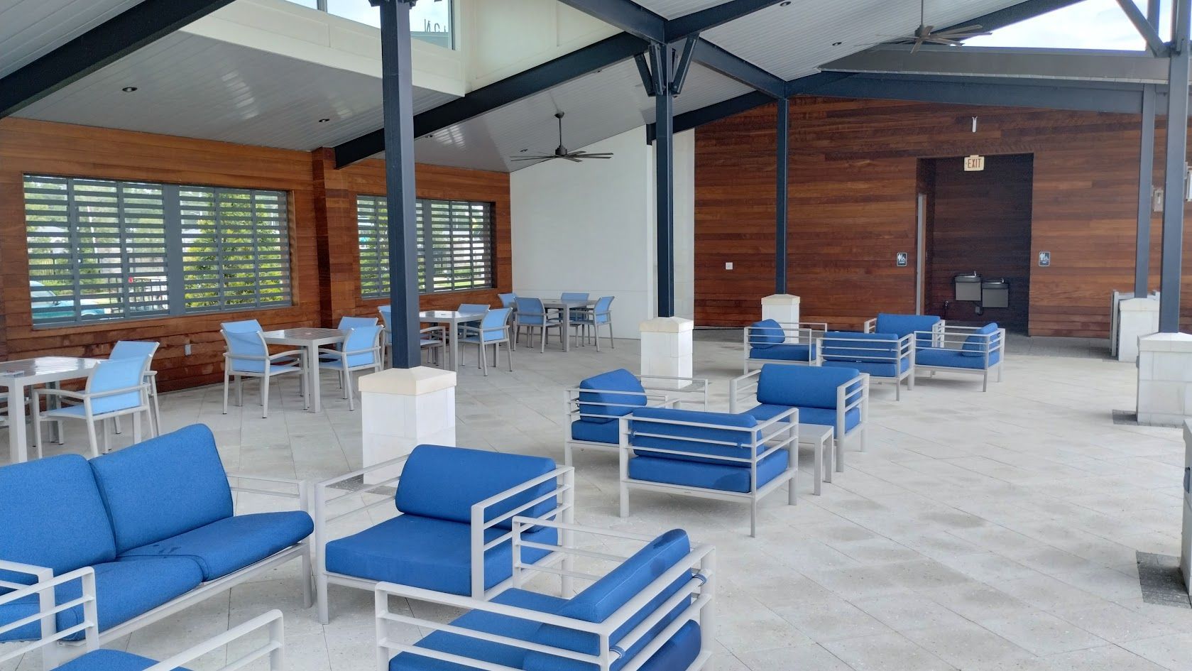 Outdoor lounge with blue seating, tables, and a wood-paneled wall.