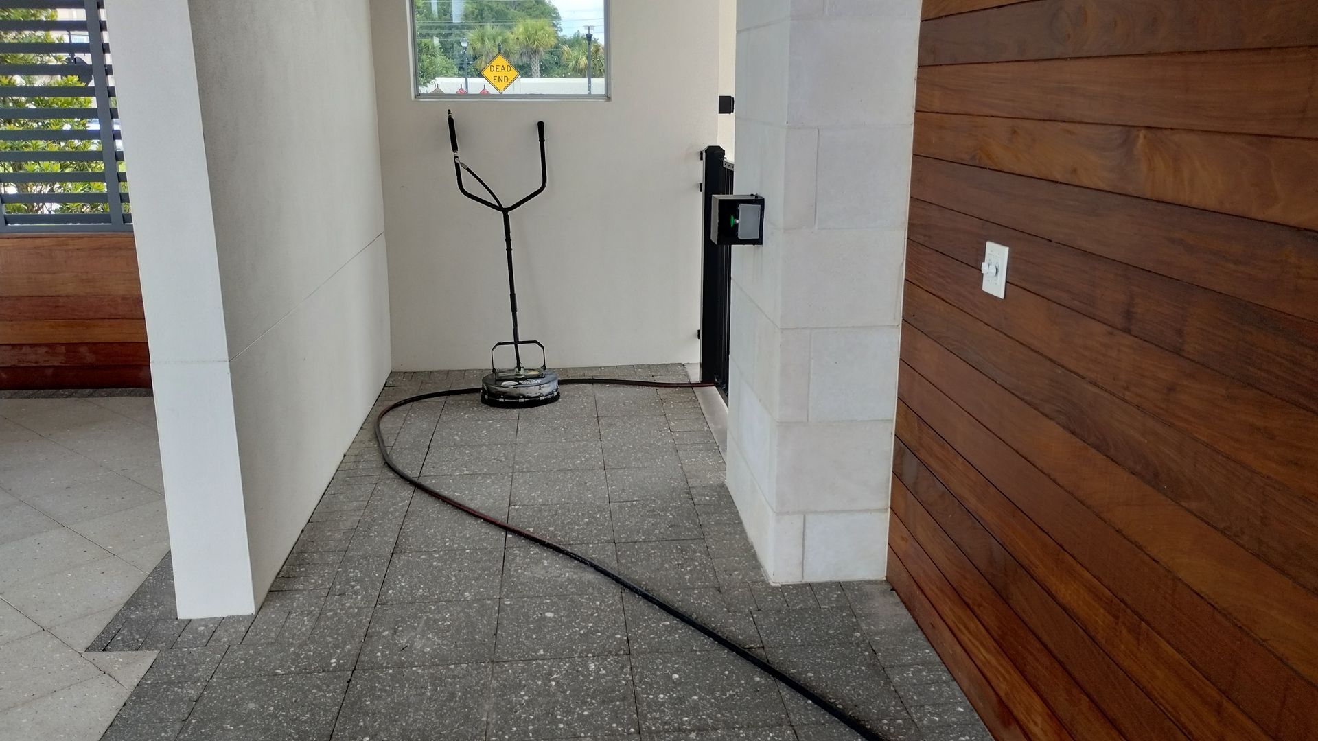 A pressure washer in a doorway, connected by a hose, beside a wooden door.