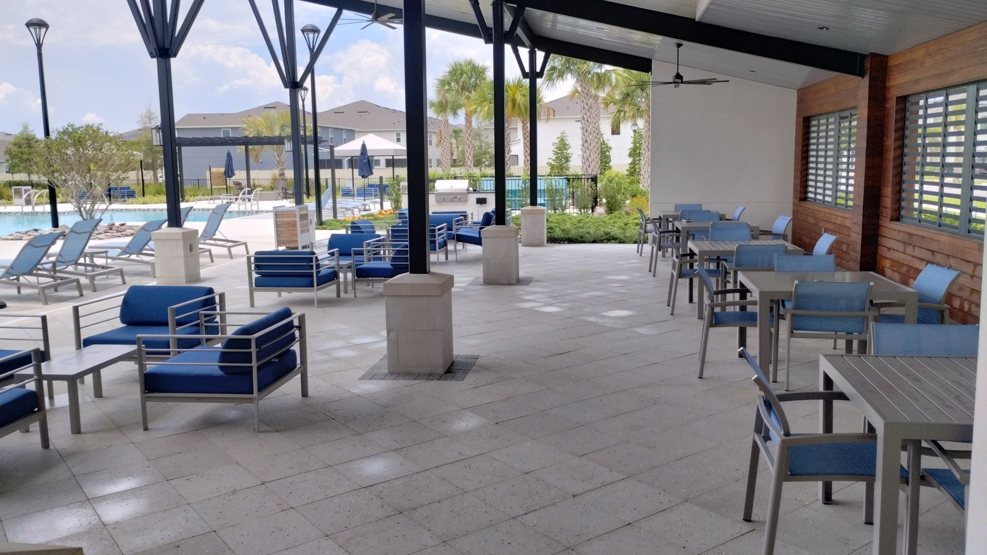 Outdoor patio with blue furniture, near a pool and brick wall.