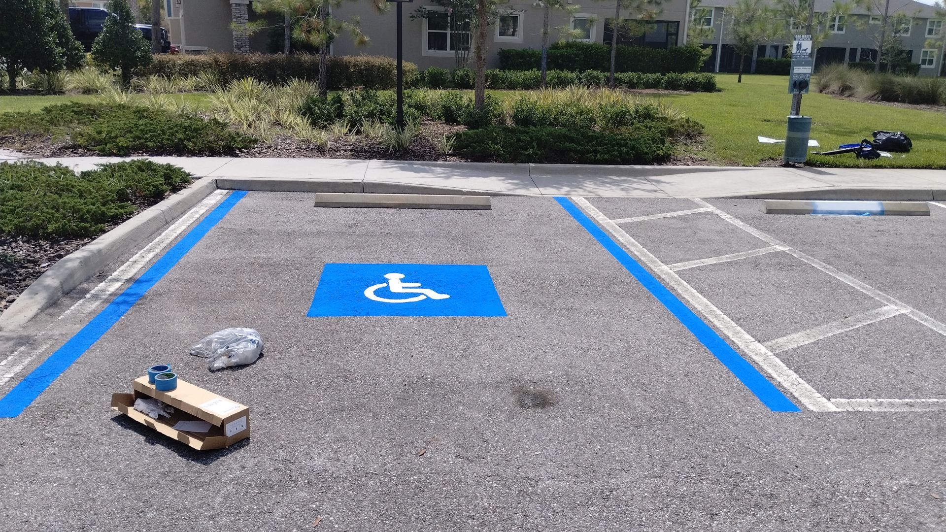 Accessible parking space painted blue with a blue wheelchair symbol. Includes a wooden object and a rock.