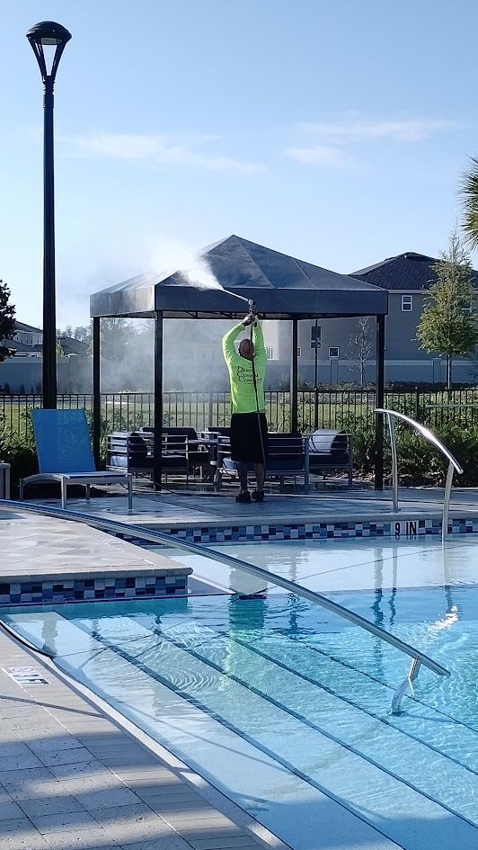 Man sprays mist onto a gazebo by a pool. He wears a neon green shirt. Sunny day.