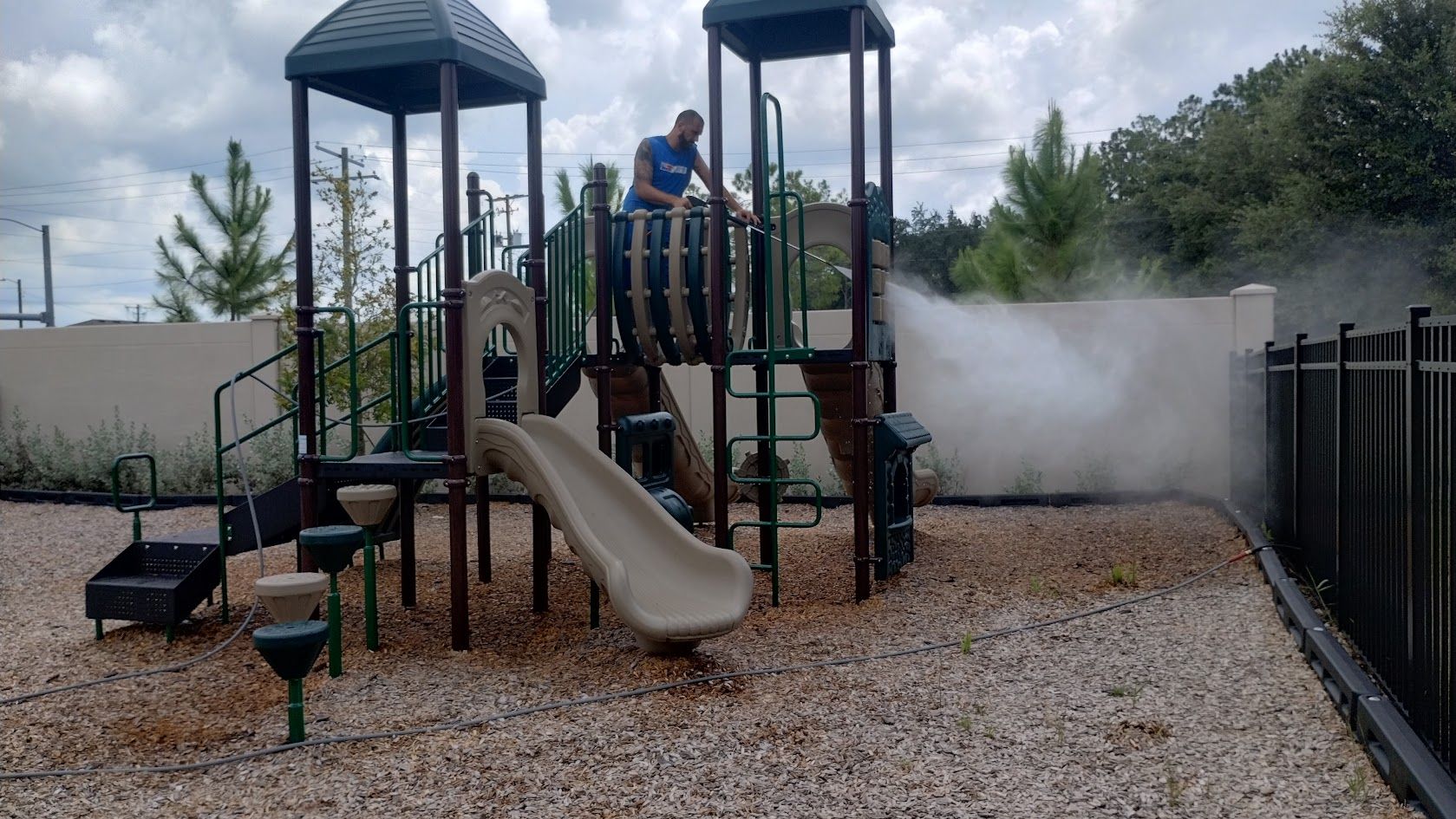 Man spraying a playground with a mist under a cloudy sky.