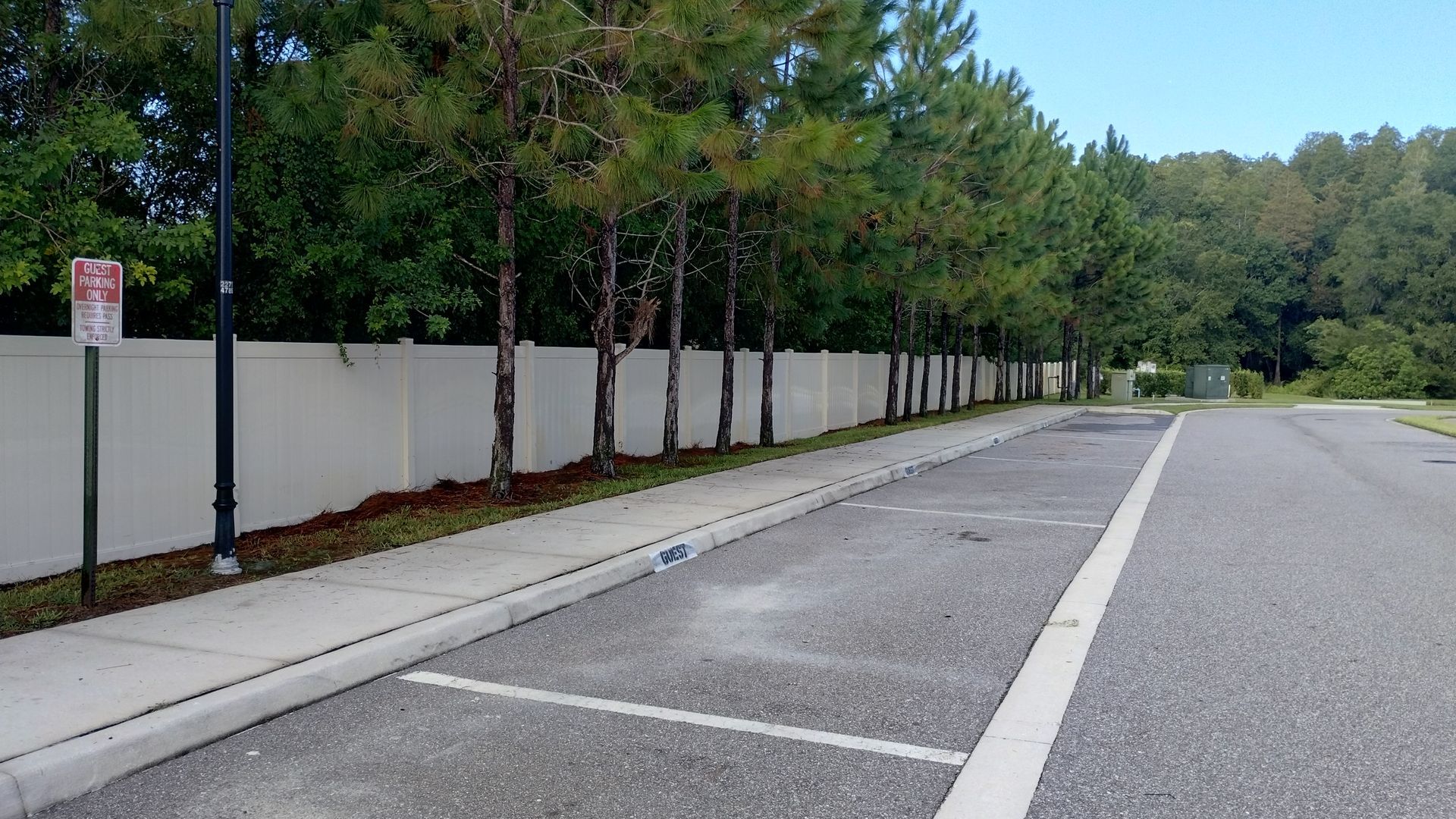 Parking lot with a white wall, trees, and a sidewalk.