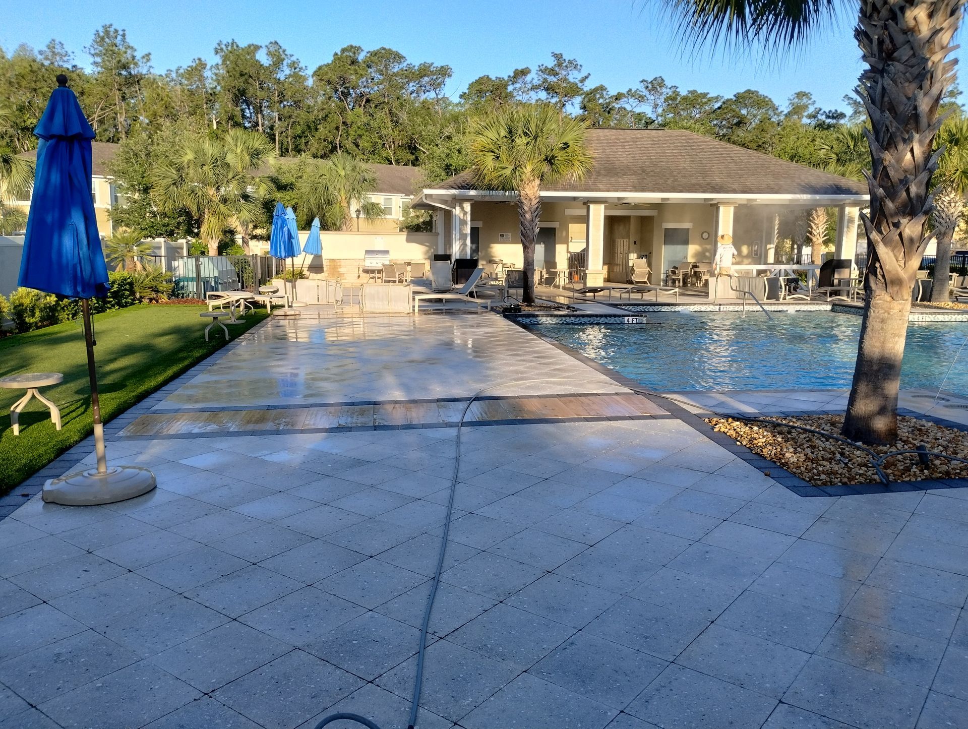 Poolside view with blue umbrellas, concrete deck, and a building in the background.
