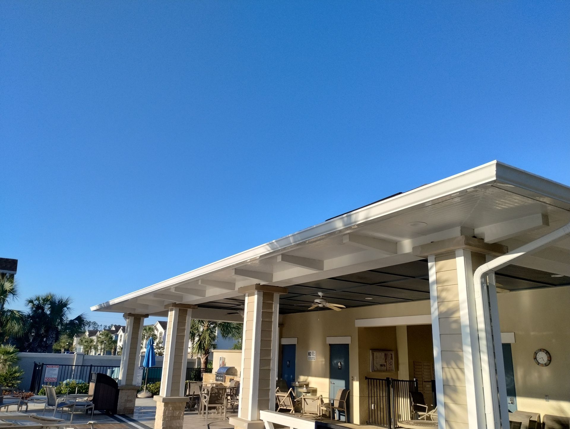 Covered outdoor area with columns, cream walls, and blue sky.