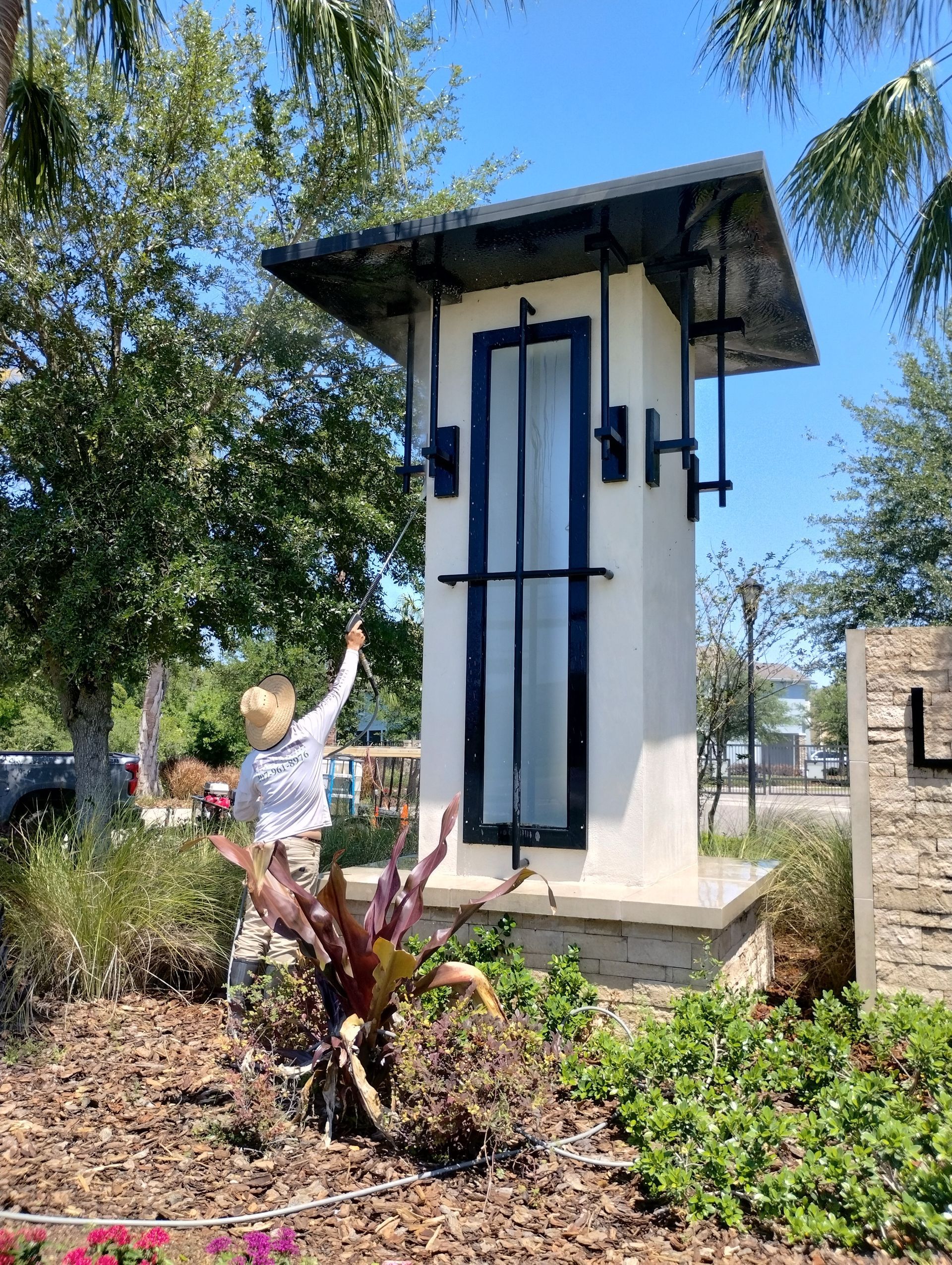 Woman points at a tall, modern entrance sign with a black roof and a central window, surrounded by landscaping.