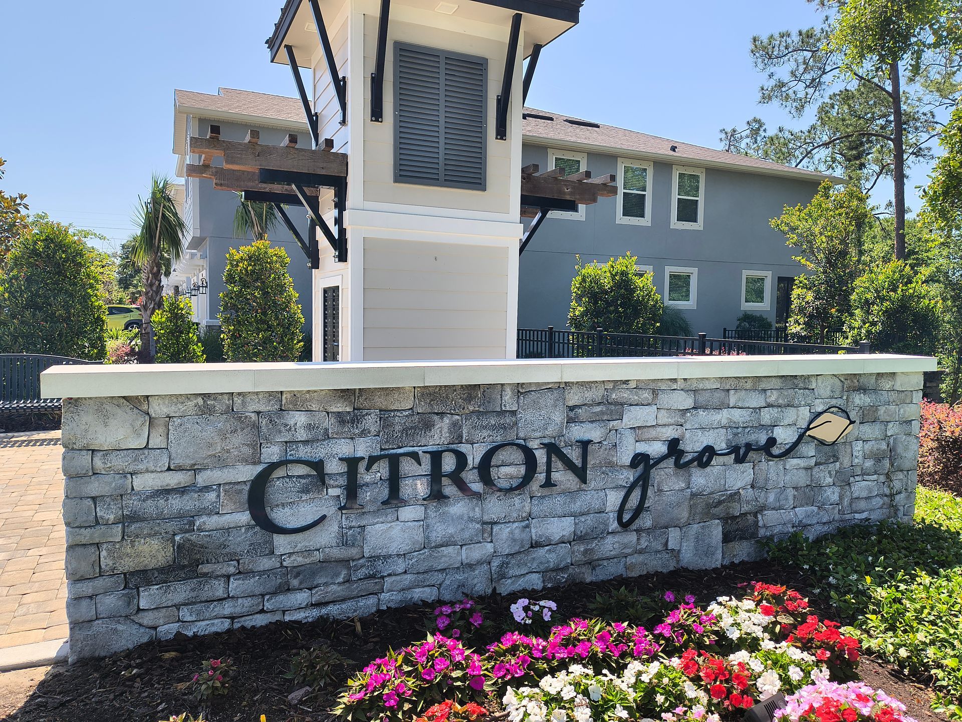 Citron Grove sign with stone facade and landscaping, background includes light blue apartments and trees.