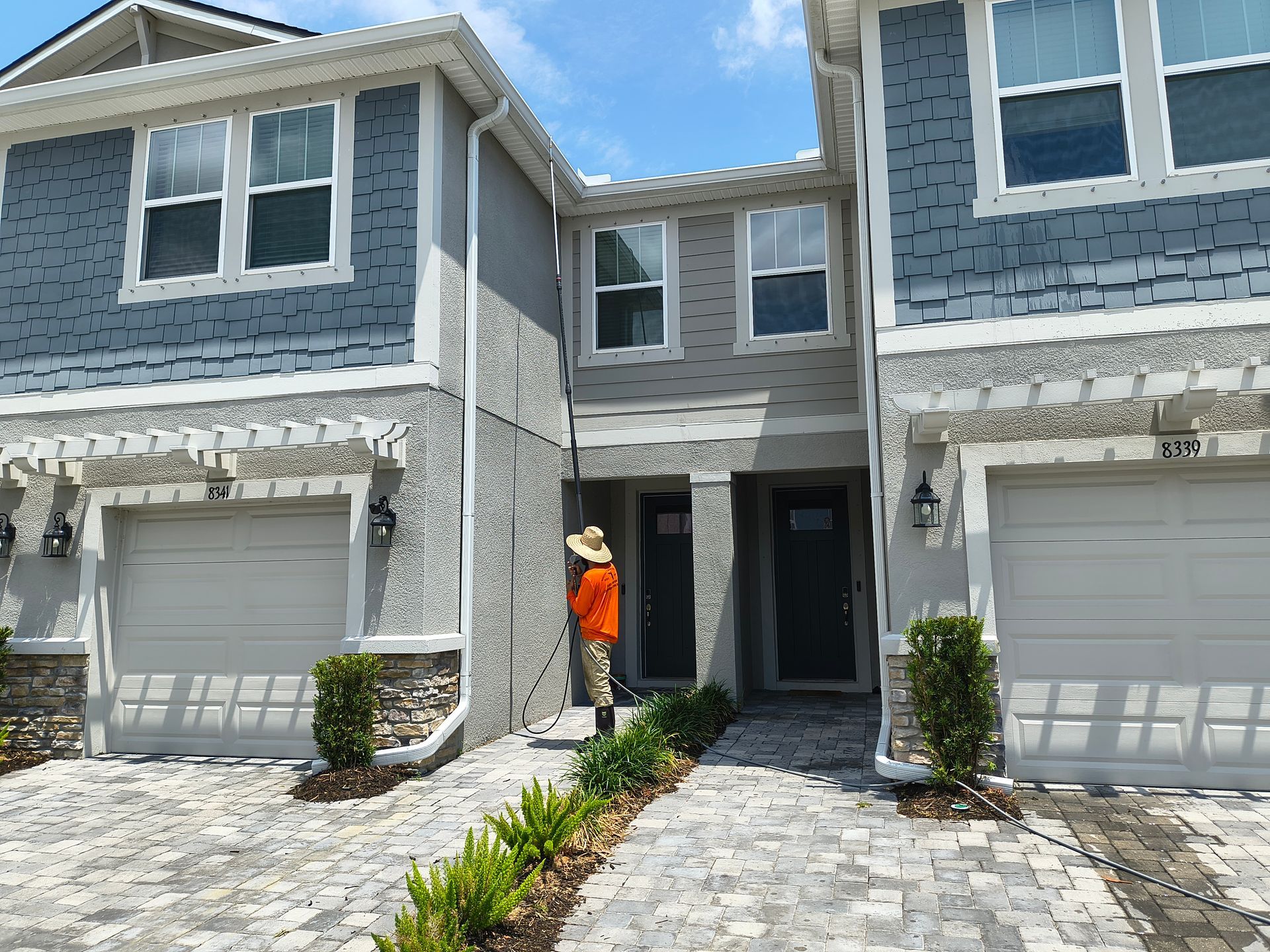 Townhouses with blue siding, gray garage doors, and a person wearing orange tending a small landscaped area.