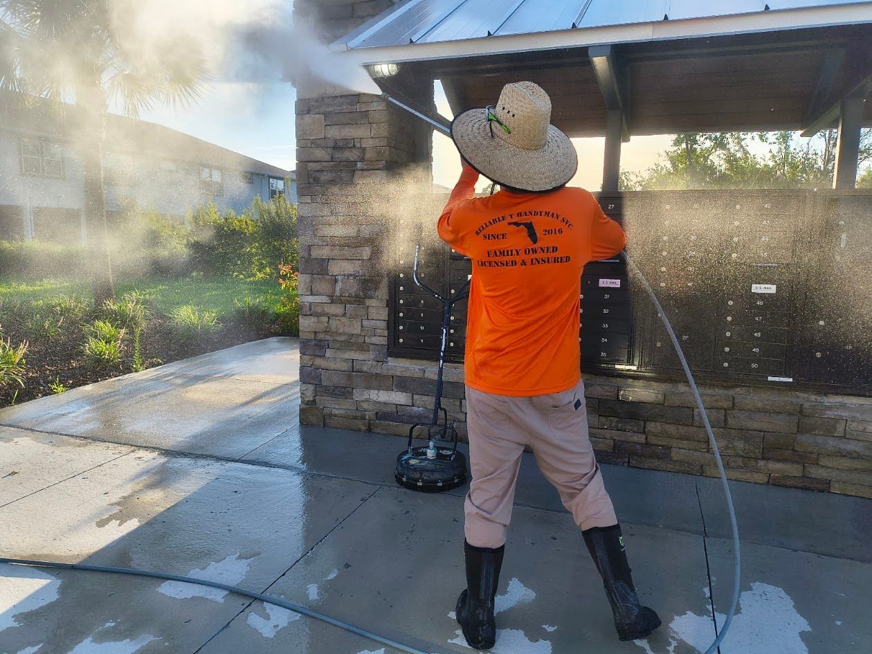 Person pressure washing a stone wall, wearing a hat and orange shirt, outdoors.