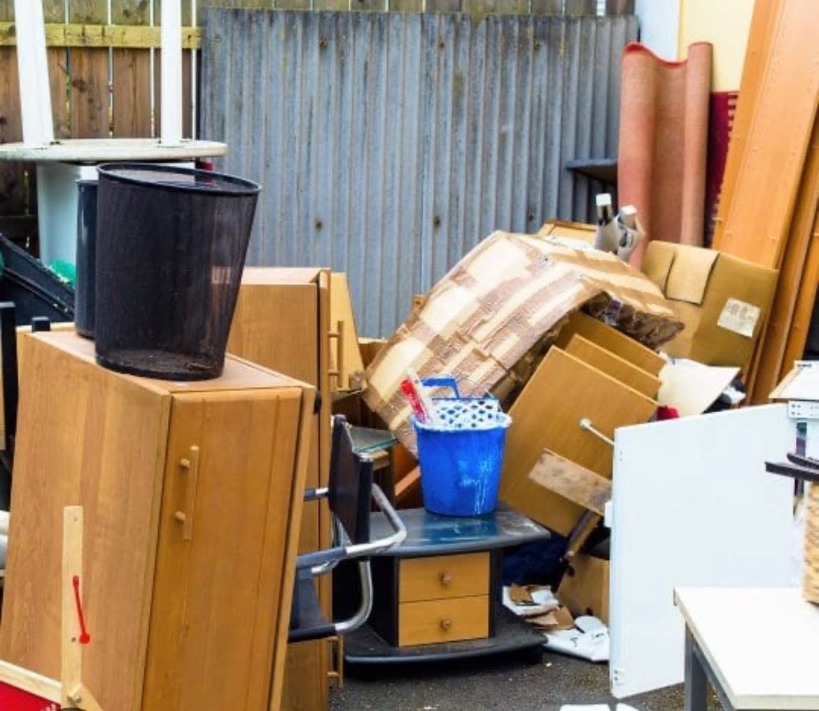 Pile of discarded furniture and boxes near a wooden fence.