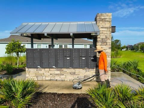 Person pressure washing a mailbox structure; sunny day, grassy area.