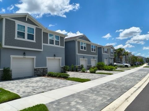 Row of modern blue and gray townhouses with white garage doors, under a blue sky.