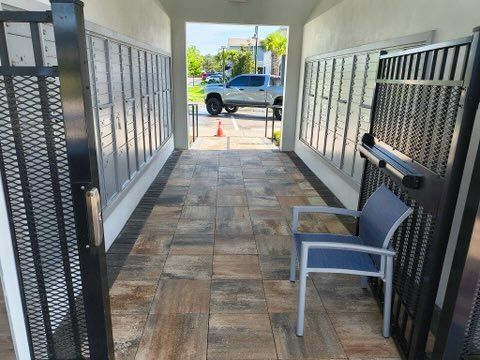 Mailboxes in a hallway, gated entrance. A chair sits inside. View of street beyond the exit.