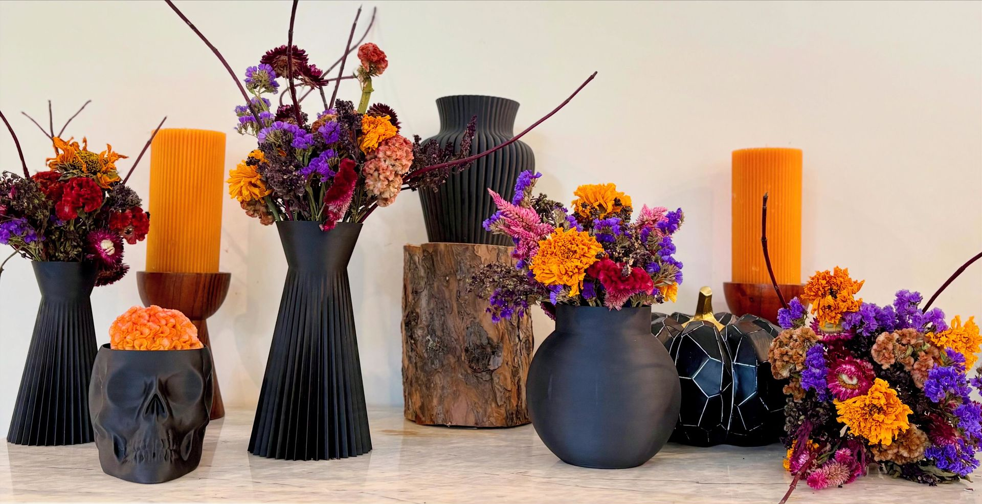 Halloween floral arrangement with black vases, orange candles, and colorful flowers.