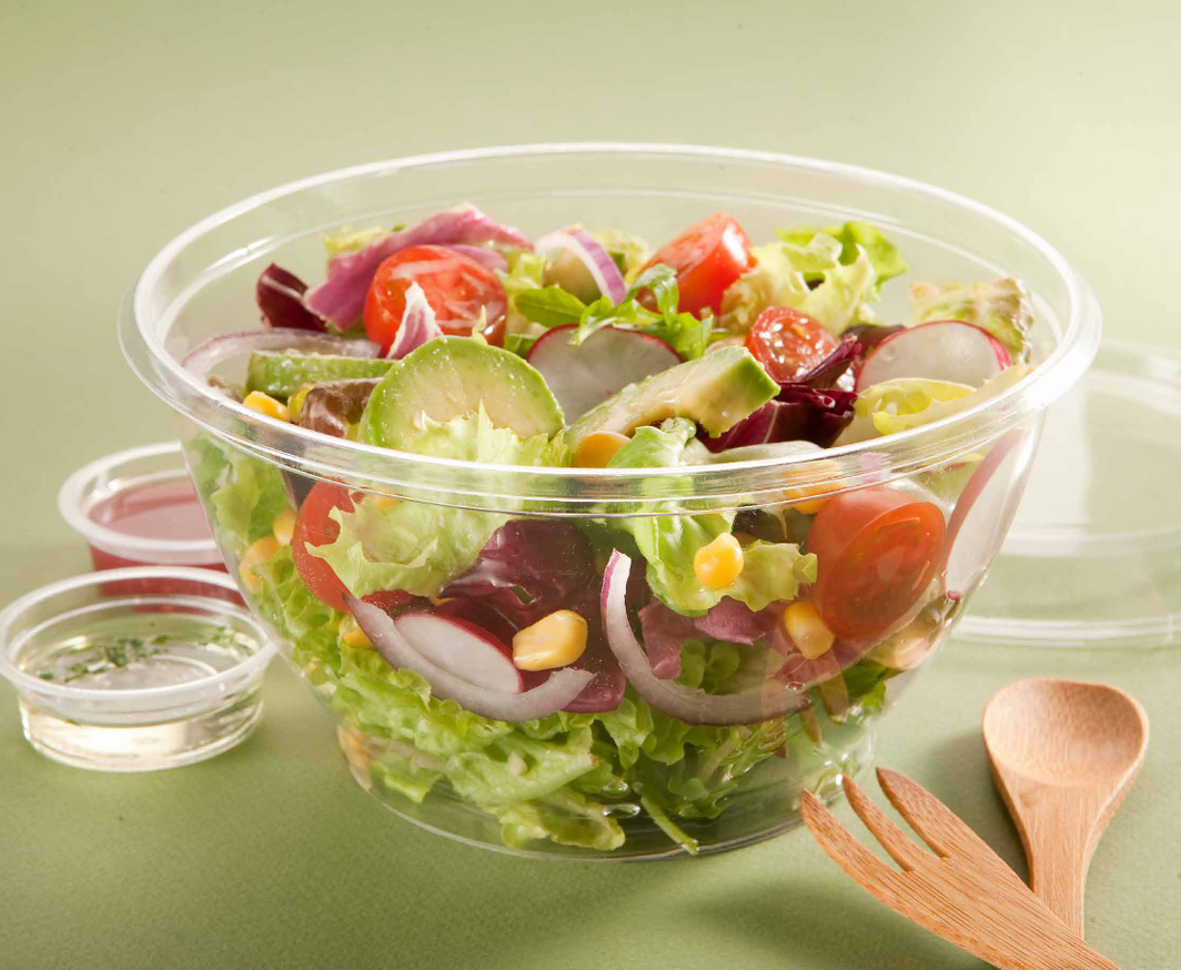Un bol de plástico transparente con ensalada mixta que incluye tomates, rábanos, maíz y lechuga
