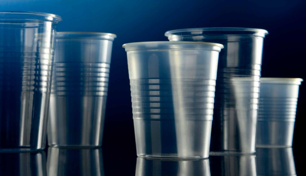 Una variedad de vasos de plástico transparentes y vacíos, con laterales acanalados, que destacan sobre un fondo azul oscuro.