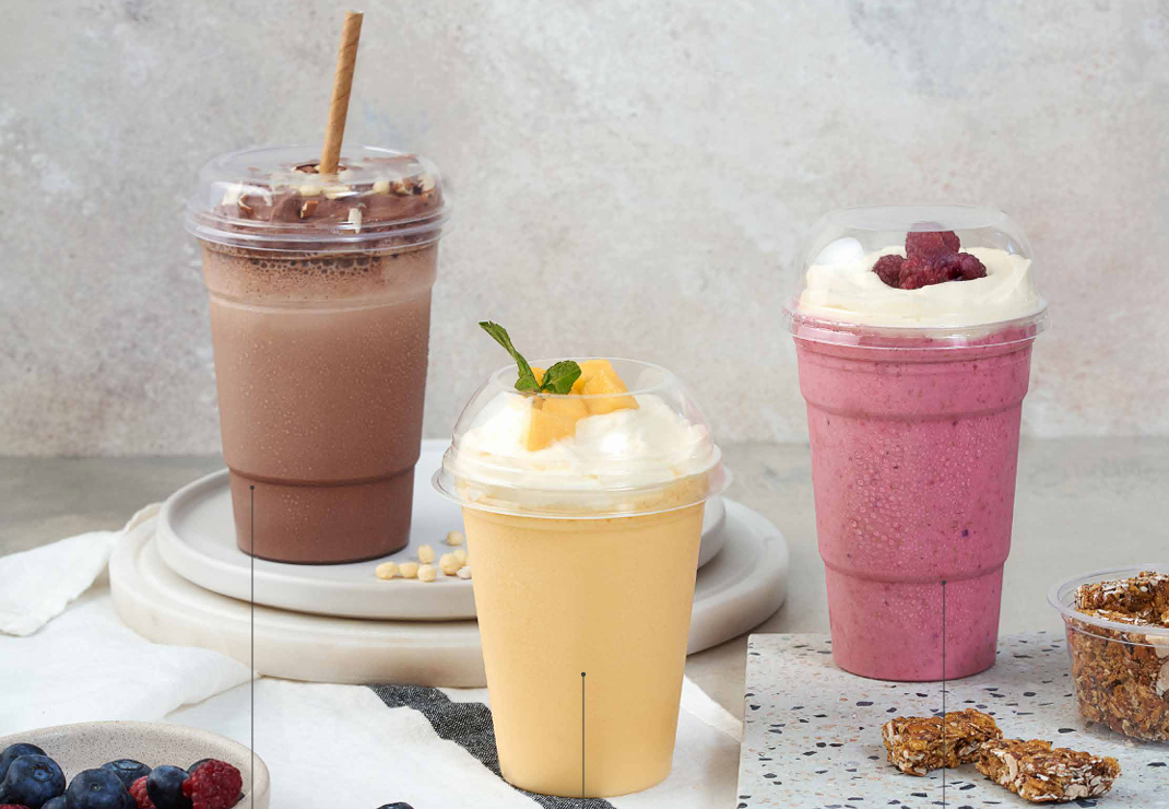 Tres vasos de plástico con batidos de chocolate, mango y frutos rojos, decorados con distintos aderezos