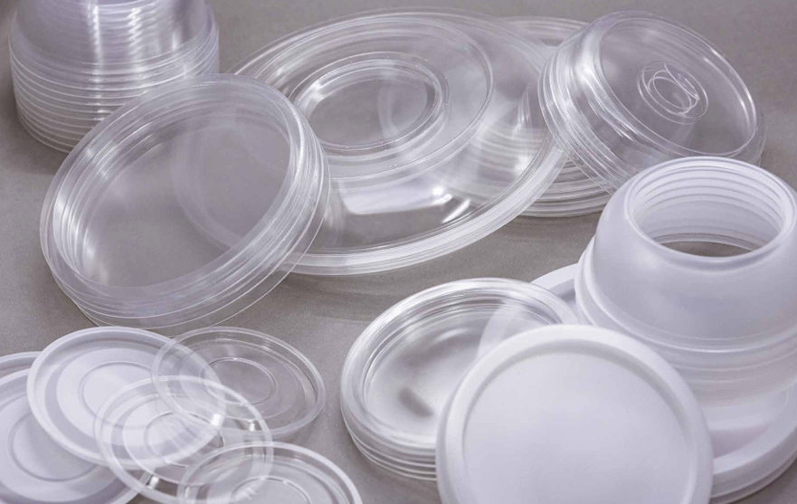 Una colección de tapas y envases de alimentos desechables de plástico transparente apilados sobre una superficie gris.