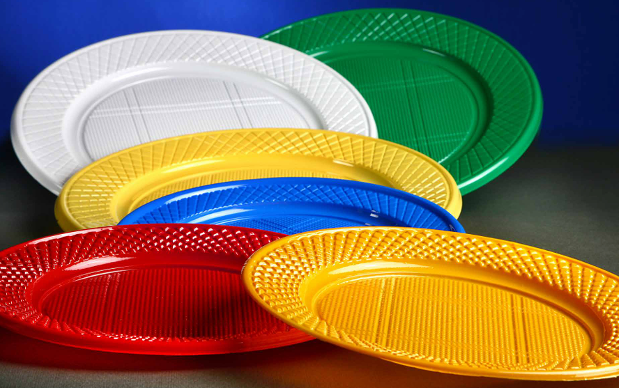 Una pila de platos de plástico de colores para fiestas: blanco, verde, amarillo, azul y rojo, sobre un fondo azul oscuro.