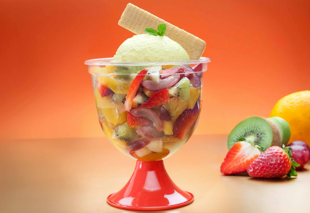 Una ensalada de frutas servida en un vaso transparente sobre una base roja