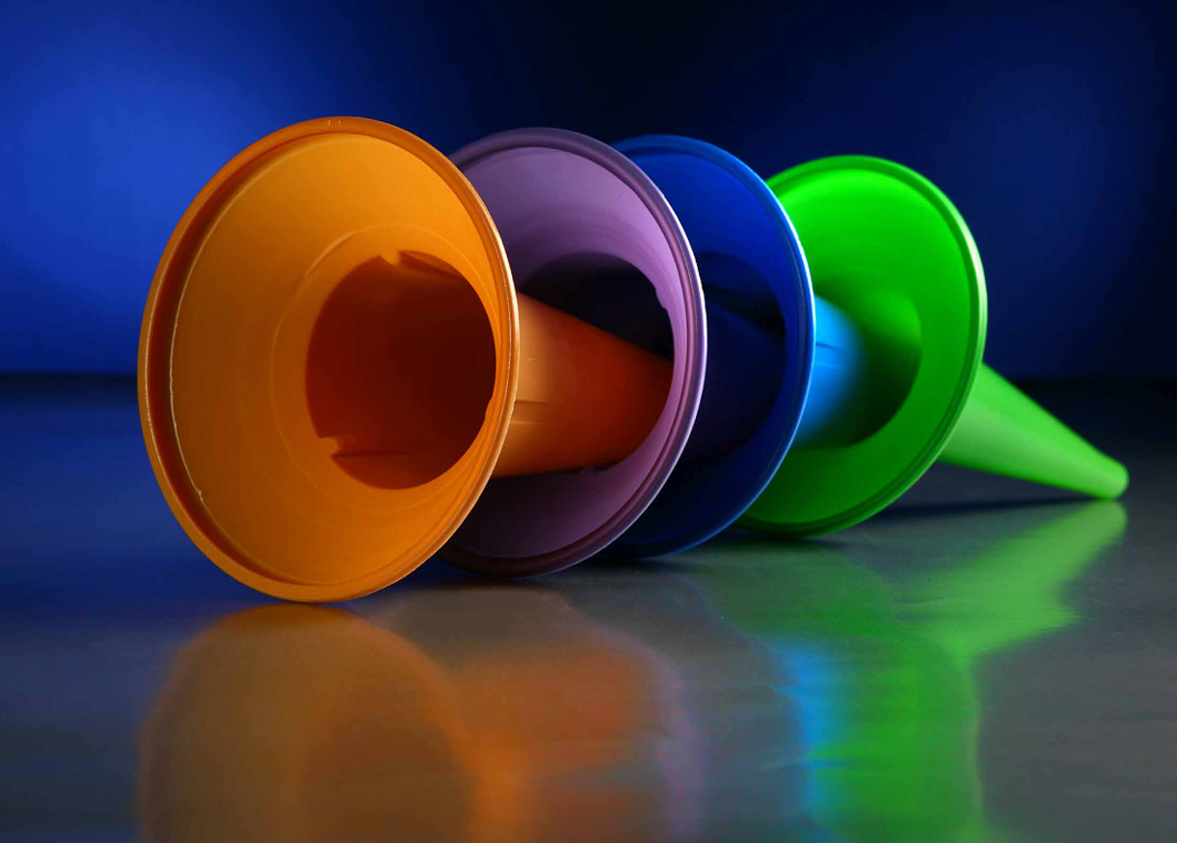 Cuatro embudos coloridos en forma de cono, alineados sobre un fondo azul oscuro con superficie reflectante.