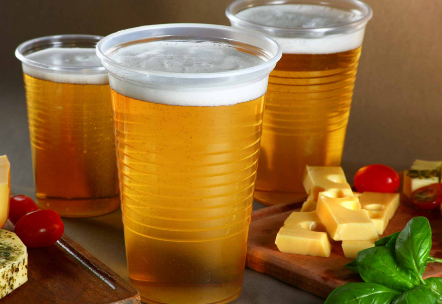 Tres vasos de plástico con cerveza espumosa, adornados con cubos de queso amarillo