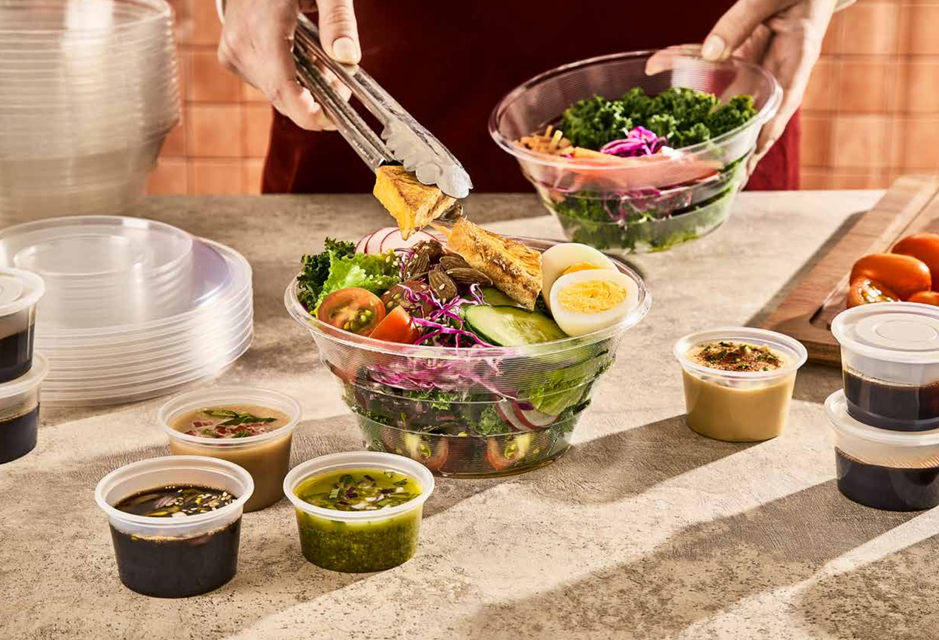 Una persona utiliza unas pinzas para colocar pollo a la parrilla sobre una ensalada fresca en un tazón