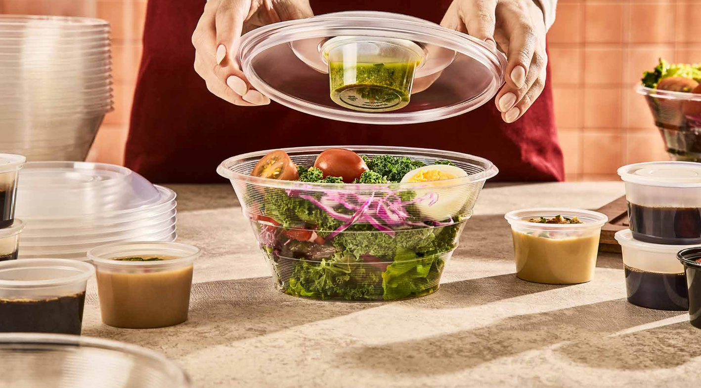 Una persona utiliza unas pinzas para colocar pollo a la parrilla sobre una ensalada fresca en un tazón