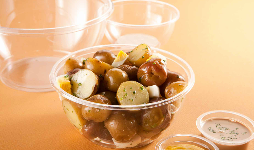 Un bol de ensalada de patatas con hierbas reposa sobre una superficie de color beige