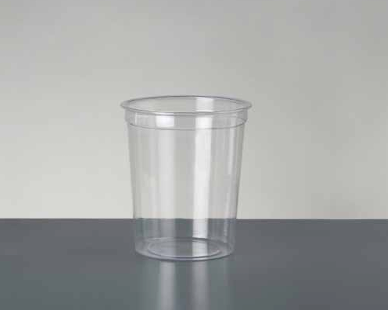 Un vaso de plástico cilíndrico, transparente y vacío, que reposa sobre una superficie gris oscuro con un fondo gris claro.