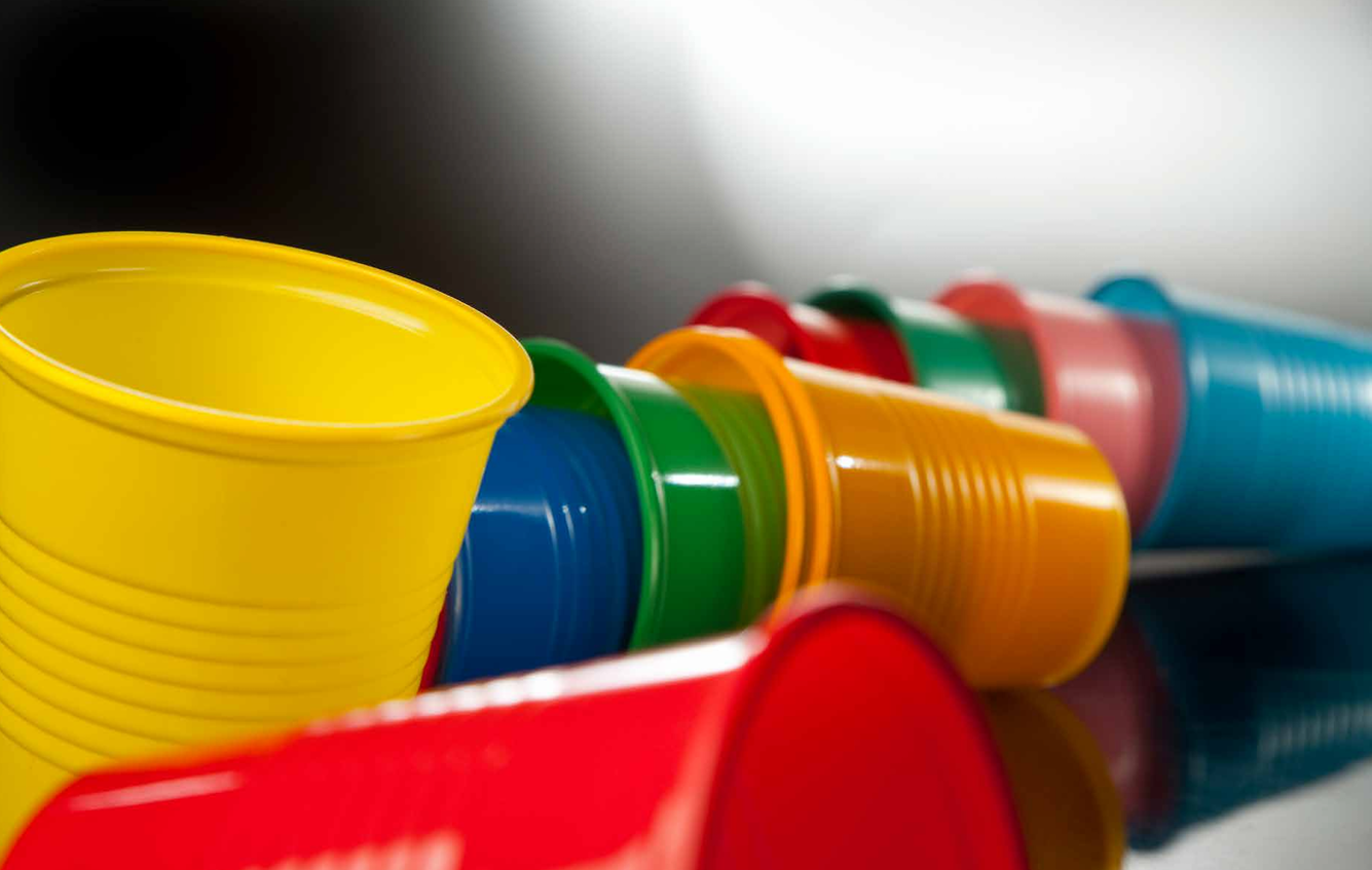 Un vaso de color amarillo brillante en primer plano, con una hilera de vasos de plástico de colores .