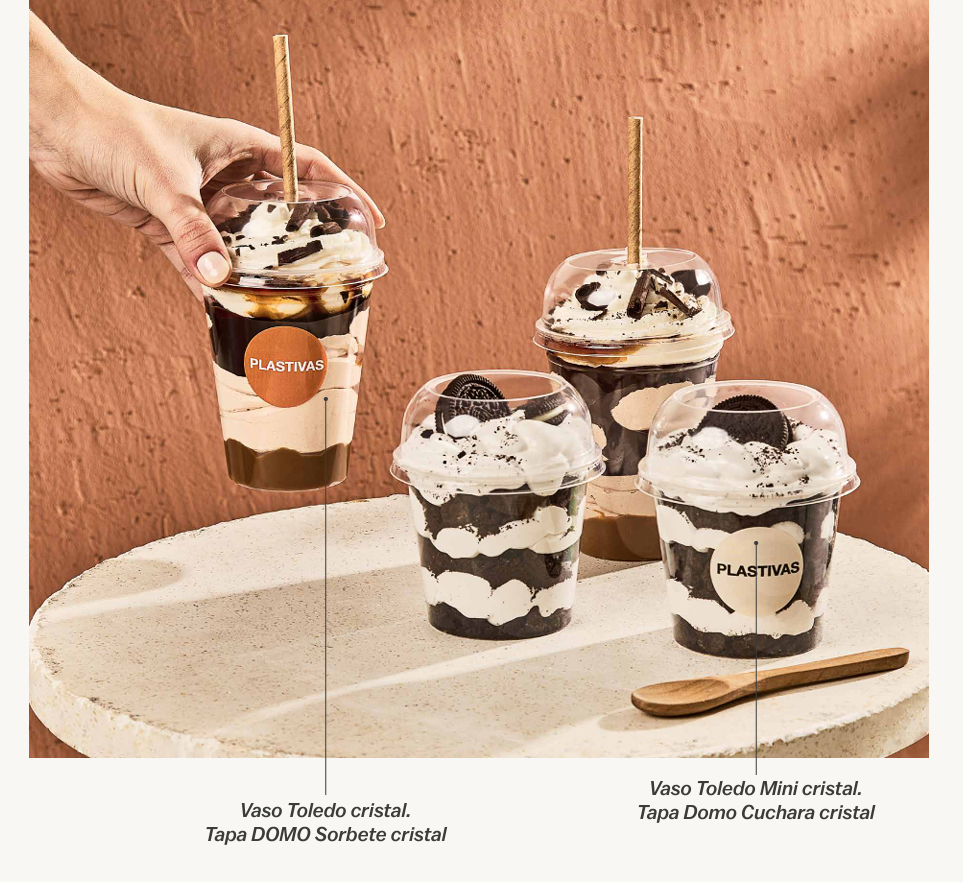 Una mano sostiene una taza alta y transparente de postre, junto a tazas más pequeñas también transparentes