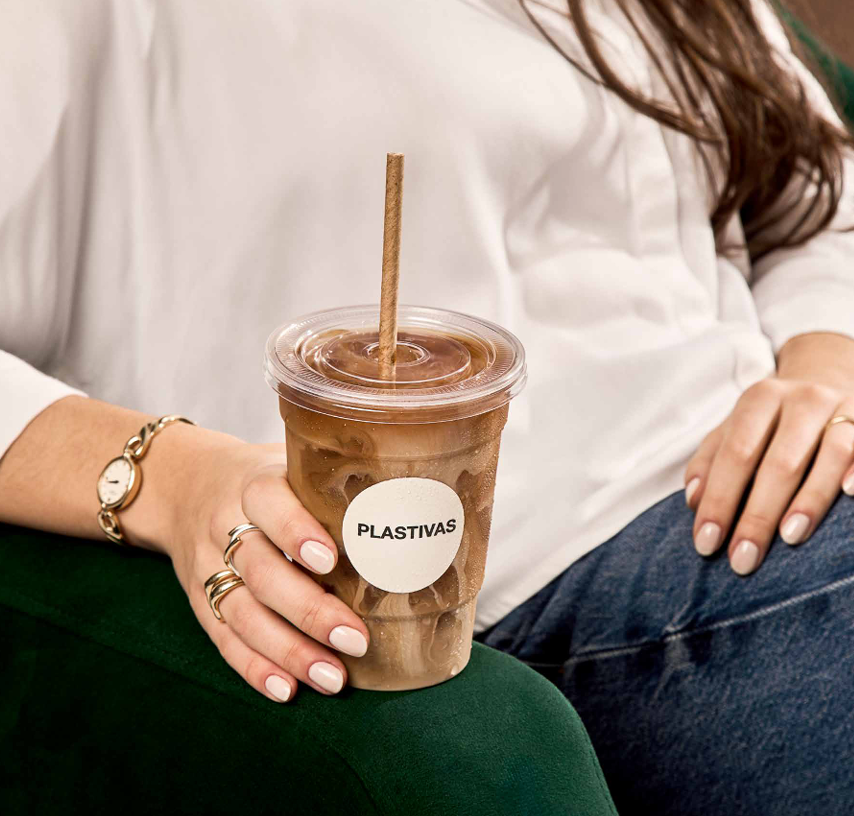 Una persona con una camisa blanca, sentada en una silla verde oscuro, sostiene un vaso de plástico
