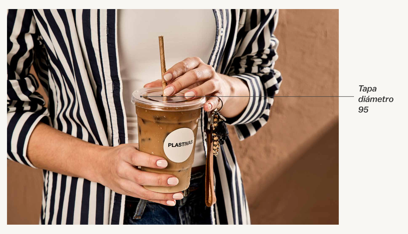 Una persona con una camisa a rayas sostiene un café helado en un vaso de plástico con tapa