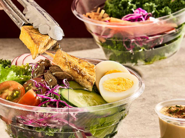 Con unas pinzas se coloca un trozo de pollo a la parrilla sobre un bol de ensalada fresca que contiene huevos duros