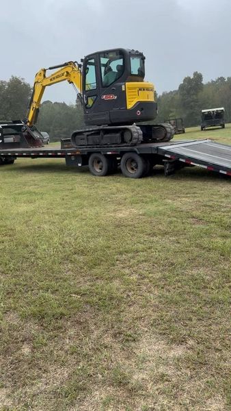 Yellow excavator on a trailer parked on a grassy field; cloudy day.