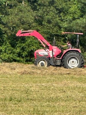 Pink tractor with a front loader, in a grassy field. A person is driving the tractor.