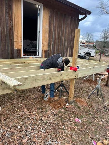 Person building a wooden deck outside a brown building, using power tools.