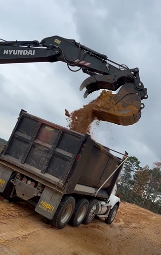 Hyundai excavator dumping dirt into a dump truck on a construction site.