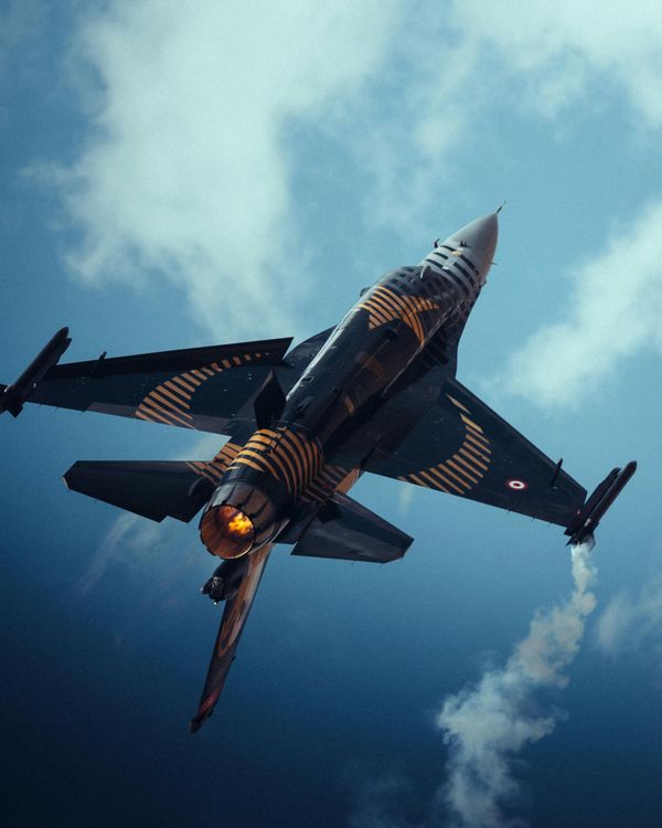 A fighter jet is flying through a cloudy blue sky