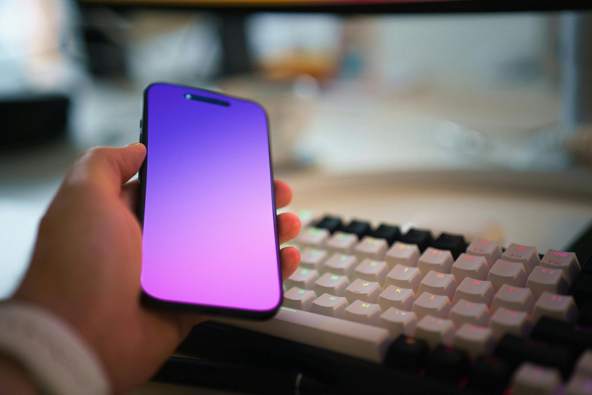 A person is holding a purple cell phone in front of a keyboard.