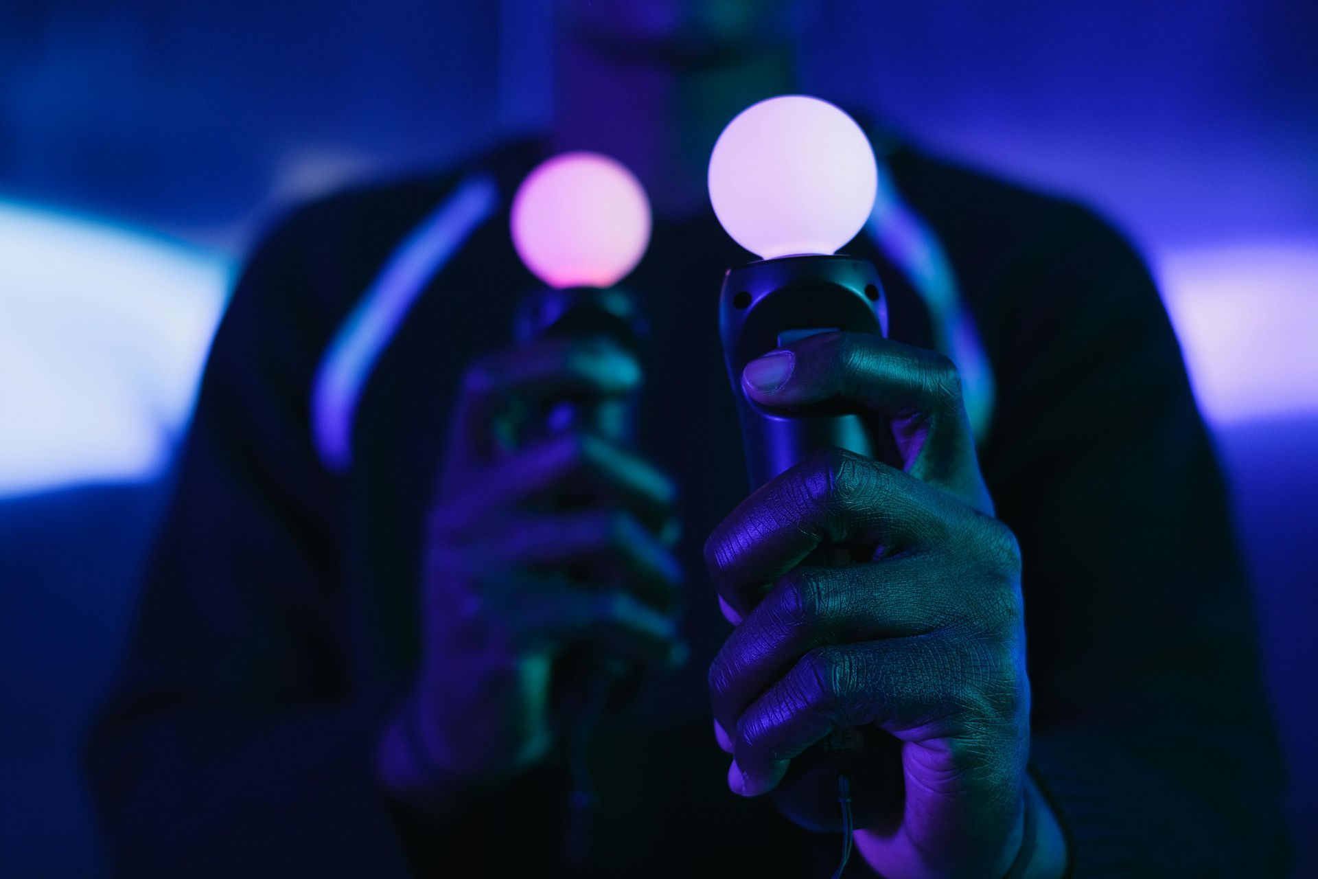 A man is holding two virtual reality controllers in his hands.