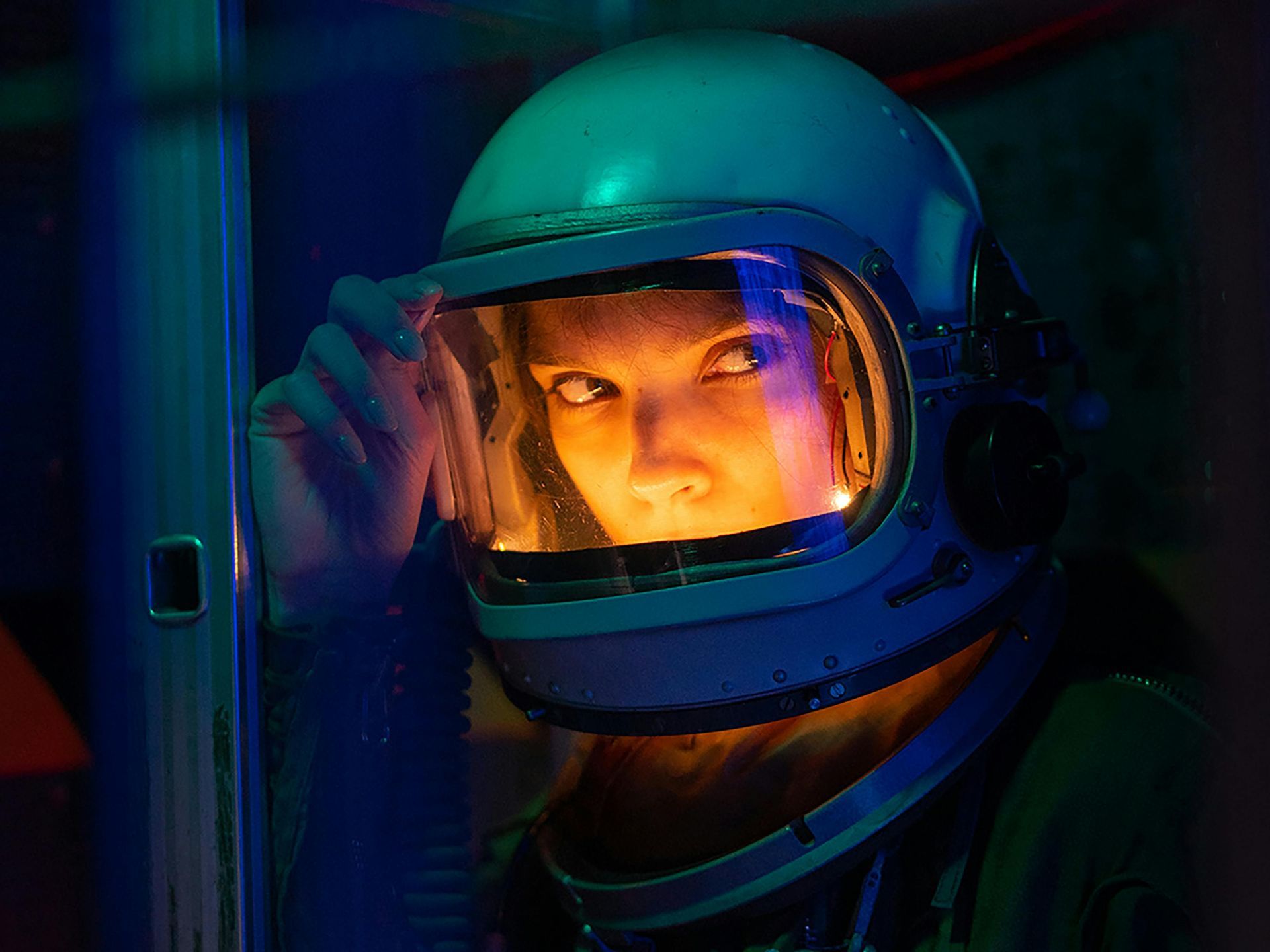 A woman in an astronaut 's helmet is looking out of a window.