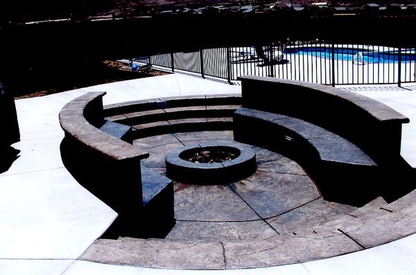 A fire pit in the middle of a patio next to a pool