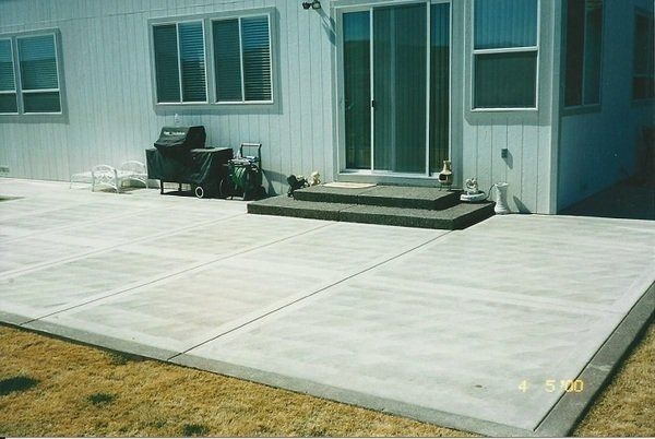 A concrete patio in front of a house with a grill and chairs