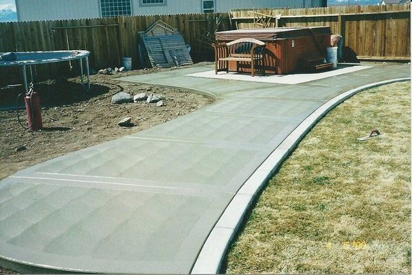 A concrete walkway leading to a hot tub in a backyard