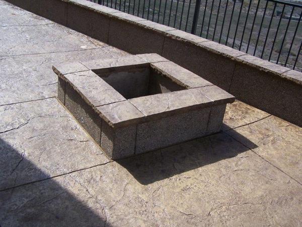 A concrete fire pit sits on a patio next to a fence