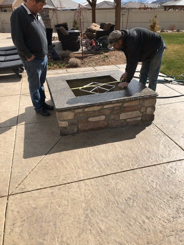 Two men are working on a fire pit on a patio.